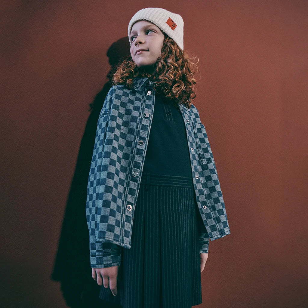 Girl wearing a stylish look with a checked jacket on a red wall.